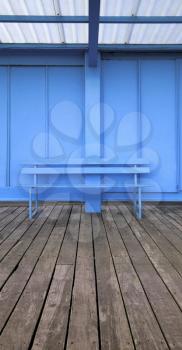 Vertical panoramic image of an empty blue bench on wooden decking