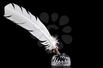 A white feather quill pen and crystal glass ink well isolated on a black background.