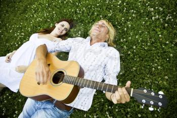 A shot of a caucasian couple lying down on the grass playing guitar and enjoying the outdoor