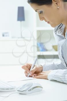 Closeup portrait of young woman writing with pen on paper, focus on hands.