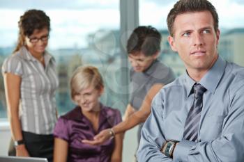 Confident businessman at office with business team in background.