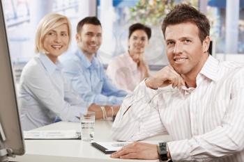 Happy businessman sitting at table in meeting room at office, looking at camera smiling