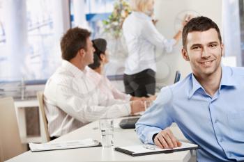 Happy young businessman in business meeting at office, looking at camera smiling.