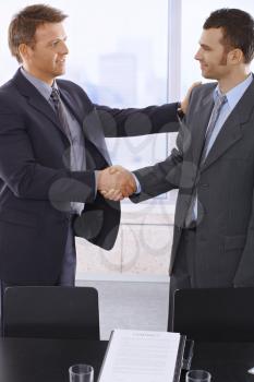Business handshake in office over signed contract.