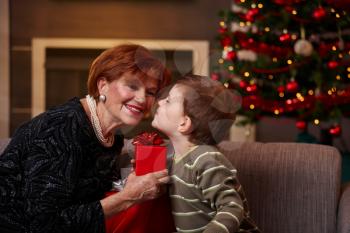 Little boy leaning to smiling grandmother with eyes closed, getting surprise christmas present.