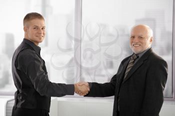 Portrait of senior executive shaking hands with young employee, looking at camera, smiling.