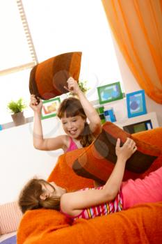 Small girls having fun in pillow fight on couch, laughing.