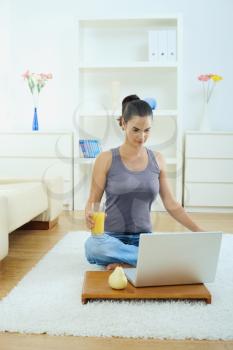 Casual young woman using laptop computer, sitting on floor in living room.