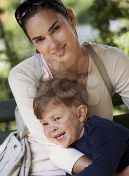 Happy mother and little boy cuddling together in park, smiling.