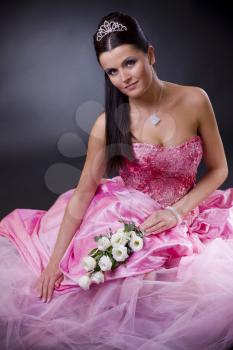 Smiling young bride sitting in a pink wedding dress, holding bouqet of white flowers.