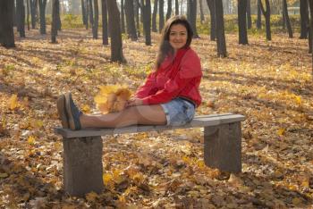 Positive girl sitting on a bench in autumn park.