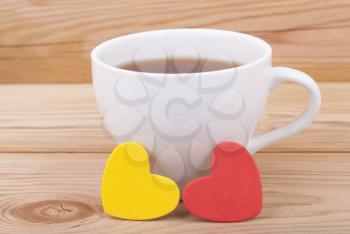 Cup of coffee and two hearts on a wooden background.