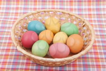 Easter colored eggs in the basket on the tablecloth.