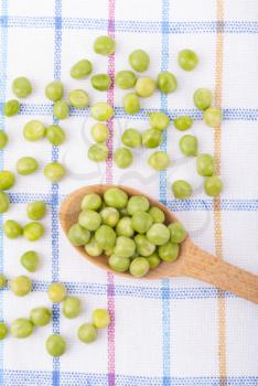 Green peas in a wooden spoon on the tablecloth.