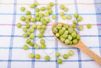 Green peas in a wooden spoon on the tablecloth.