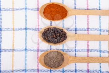 Whole and ground pepper in a wooden spoon on the tablecloth.