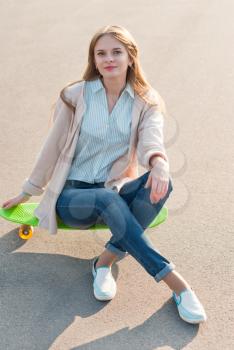 Young girl sitting on a skateboard in the street.