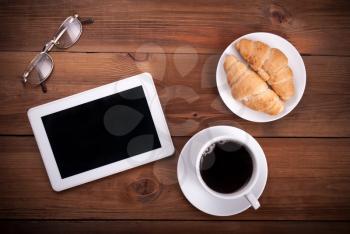 Tablet computer croissants cup of coffee glasses on a wooden background. Top view .