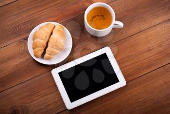Cup of tea tablet croissants on a wooden table.