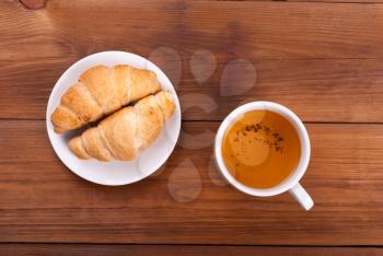 Cup of tea and croissants on a wooden background.