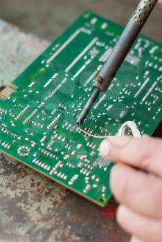 Man with soldering iron to solder electronic board.