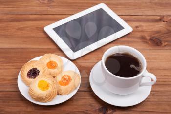 Cup of coffee and sweet cakes digital tablet on the table.