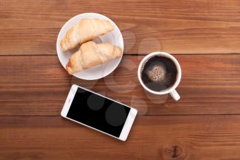 Cup of coffee and croissants mobile phone on a wooden table.