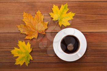 Cup of coffee and maple leaves on a wooden table.