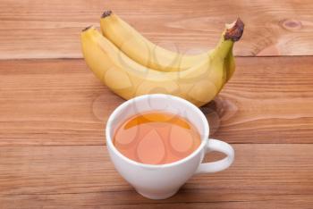 Cup of tea and bananas on a wooden background.