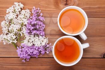 Two cups of tea and lilac flowers on a wooden background.