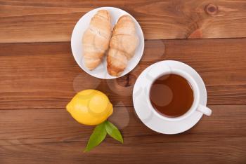 Cup of tea lemon and croissants on a wooden background. View from above .