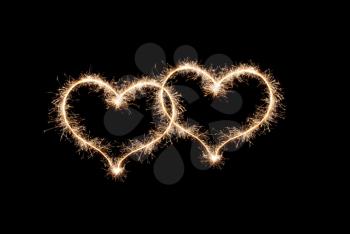 Two hearts a love symbol made by sparklers on a black background.