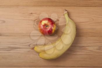 Apple and ripe bananas lie on a wooden background.