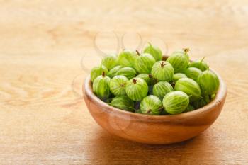 Old Wooden Bowl Filled With Succulent Juicy Fresh Ripe Green Gooseberries On An Old Wooden Table Top.