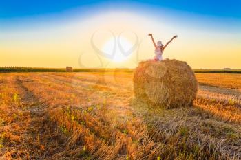 Beautiful Young Girl Sitting On Haystack And Greets Sun At Sunset, Sunrise