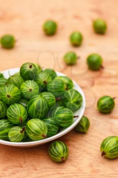 White Dish Filled With Succulent Juicy Fresh Ripe Green Gooseberries On An Old Wooden Table Top.