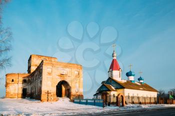 Red Brick Walls Of Old Ruined Orthodox Church Of The St. Nicholas Near New Church In Village Lenino, Dobrush District, Gomel Region, Belarus. Sunset At Winter Season. Sunny Day With Blue Sky.