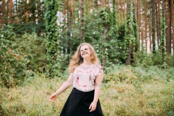 Young Pretty Plus Size Caucasian Happy Smiling Laughing Girl Woman With Wavy Brown Long Hair In White T-Shirt, Waltz Round In Summer Green Forest.