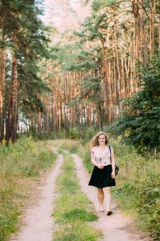 Young Pretty Plus Size Caucasian Happy Smiling Girl Woman In White T-Shirt And Black Short Skirt Walking Full-Length On Road In Summer Pine Forest