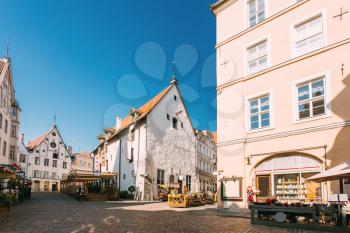 Tallinn, Estonia. People Resting In Street Cafe Restaurant And Walking In Old Town Under Facades Of Buildings. Tourists Walking Near Town Hall Square In Sunny Summer Day With Blue Sky