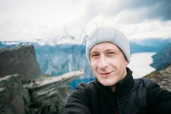 Young Tourist Taking Selfie Against The Backdrop Of The Norwegian Mountains Trolltunga. Troll's Tongue Rock Above Lake Ringedalsvatnet, Norway