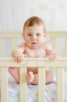 naked child sitting in a crib and looking at the camera
