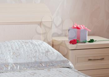 gift box with a pink tape and red rose lie on a bedside table in a bedroom