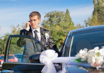 the groom speaks by phone near dressed up the wedding car
