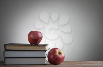 Stack of books and red apples on wooden table