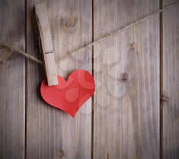 red heart made of paper with clothespin hanging on a rope and wooden planks background with space for text