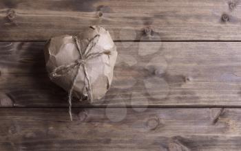 Heart wrapped in brown kraft paper, on wooden background