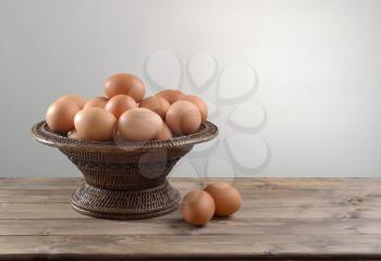 pile of chicken eggs in a wicker bowl on wooden table