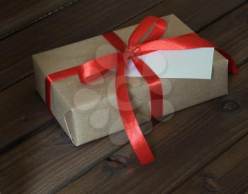 Vintage gift box wrapped in kraft paper and red ribbon on wooden background