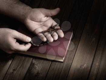 wooden Christian cross in his palms on the Bible during prayer.